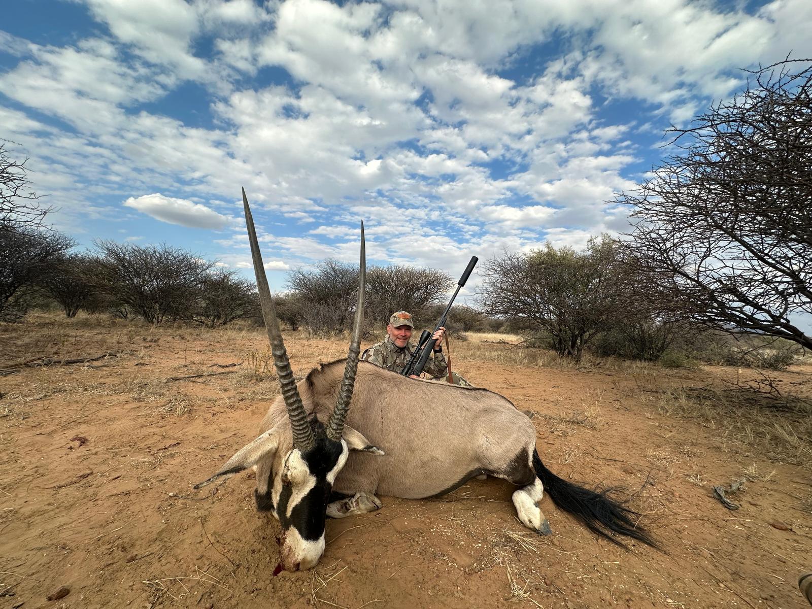 A hunter with a harvested oryx in dry scrub under a heavy cloudy sky