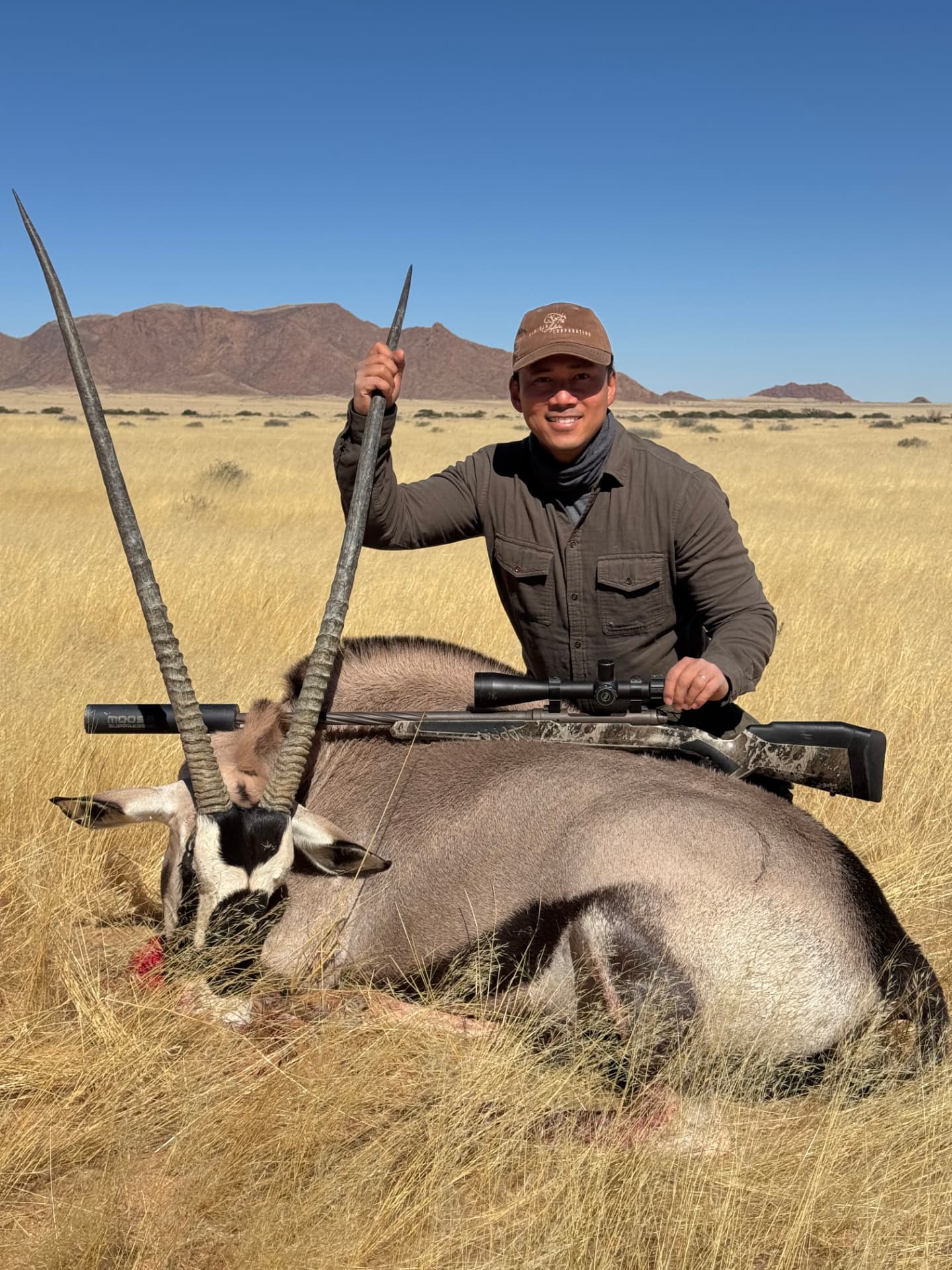 A smiling hunter beside a harvested gemsbok in open dry grassland