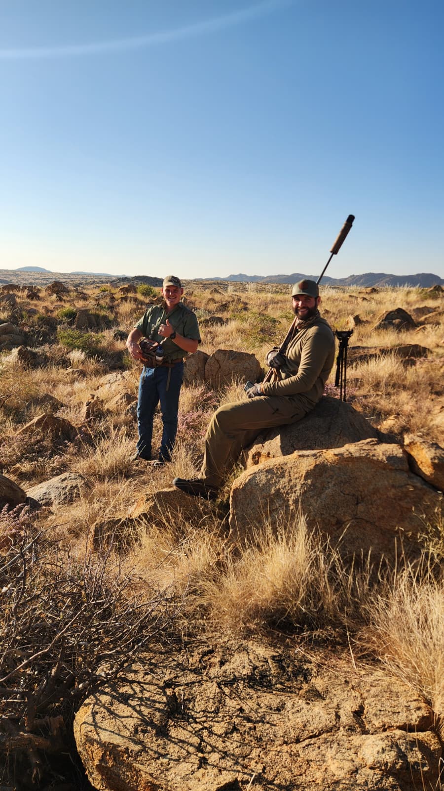 Two hunters resting on large sunlit boulders while glassing the valley below