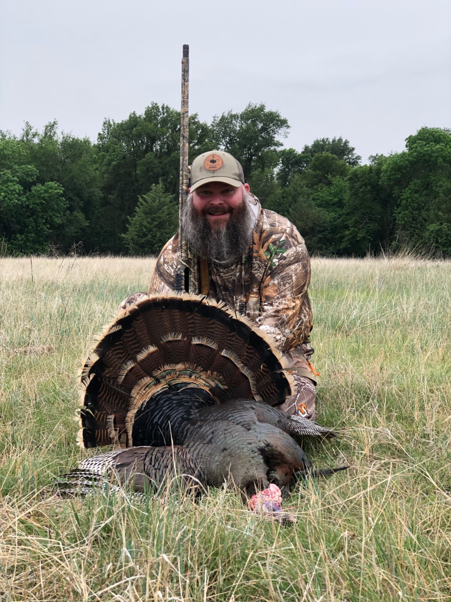 A hunter in camouflage kneeling in a grassy field with a harvested turkey