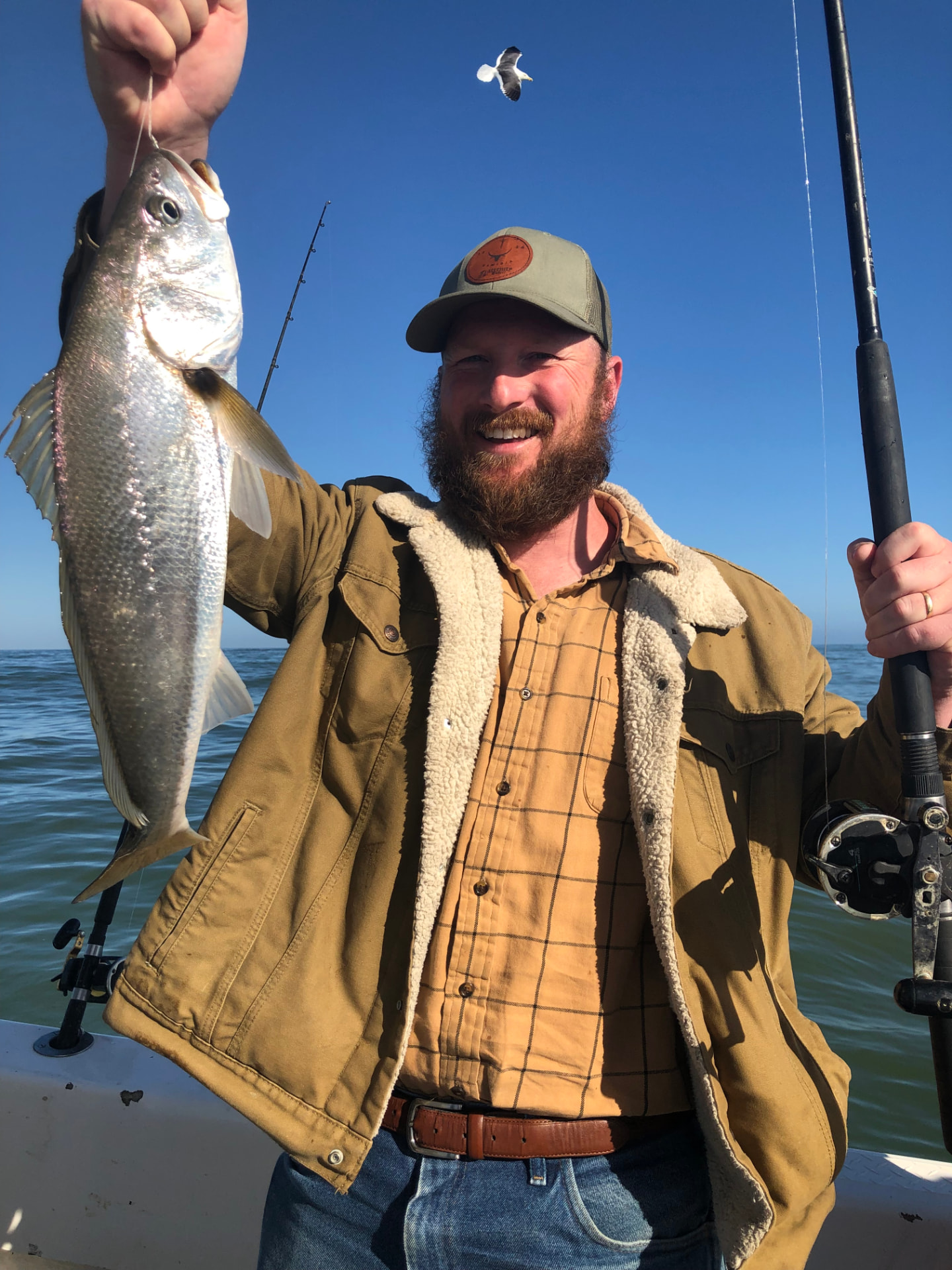 A grinning angler holding up a large fish on the deck of a boat at sea