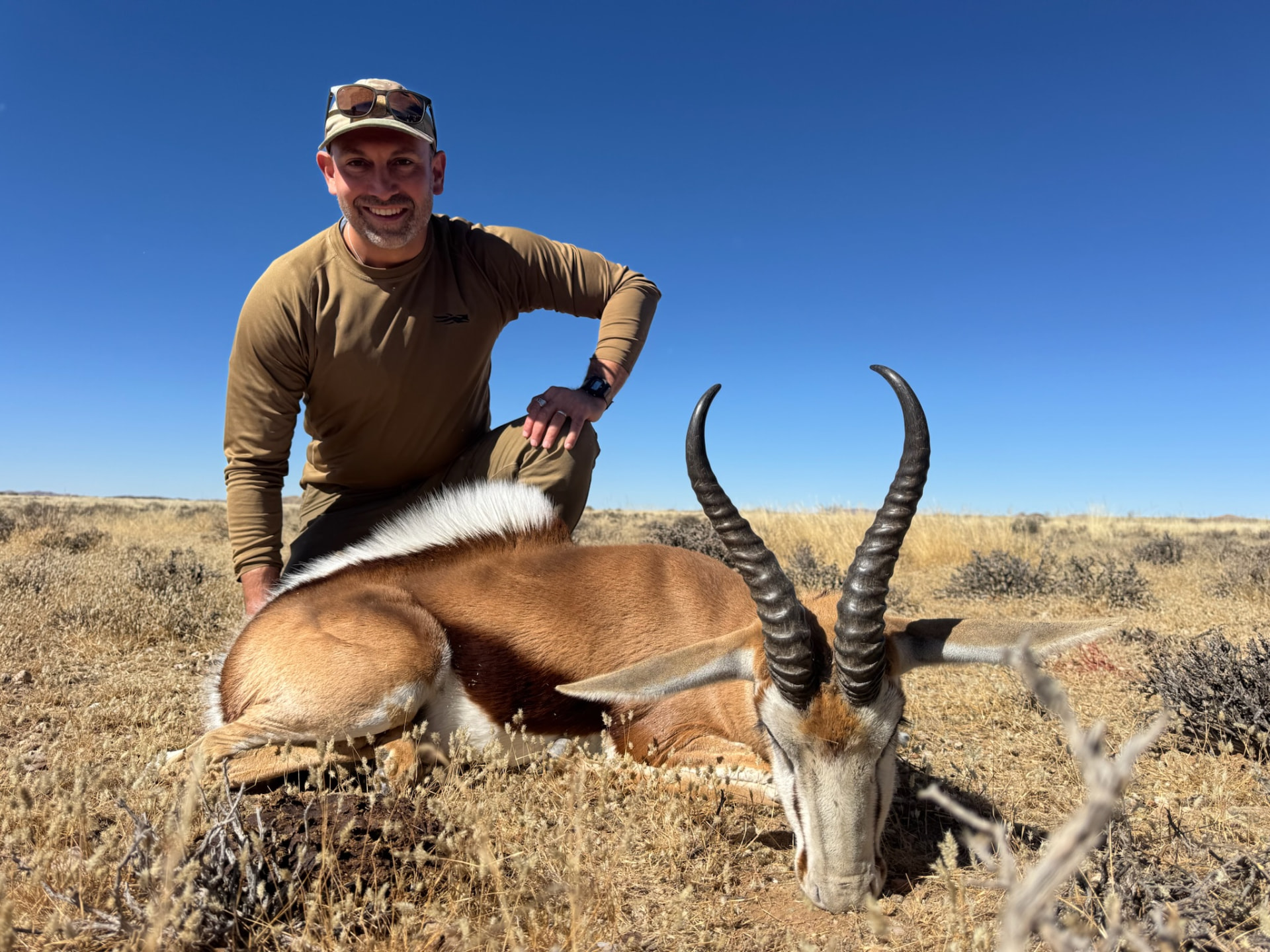 A hunter kneeling in open desert terrain beside a harvested springbok